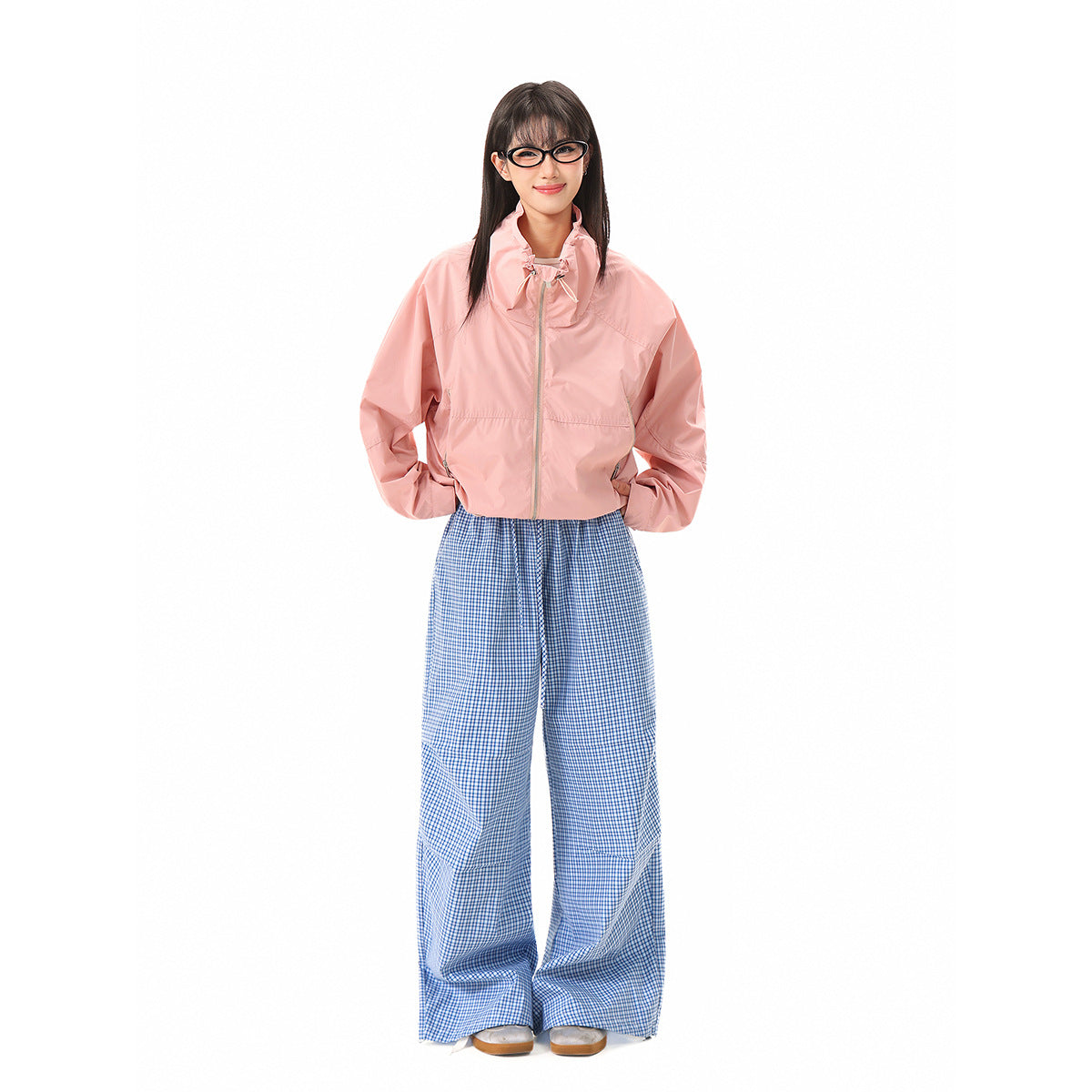 A model wears a light pink zip jacket with a high collar and blue-and-white checked wide-leg trousers.
