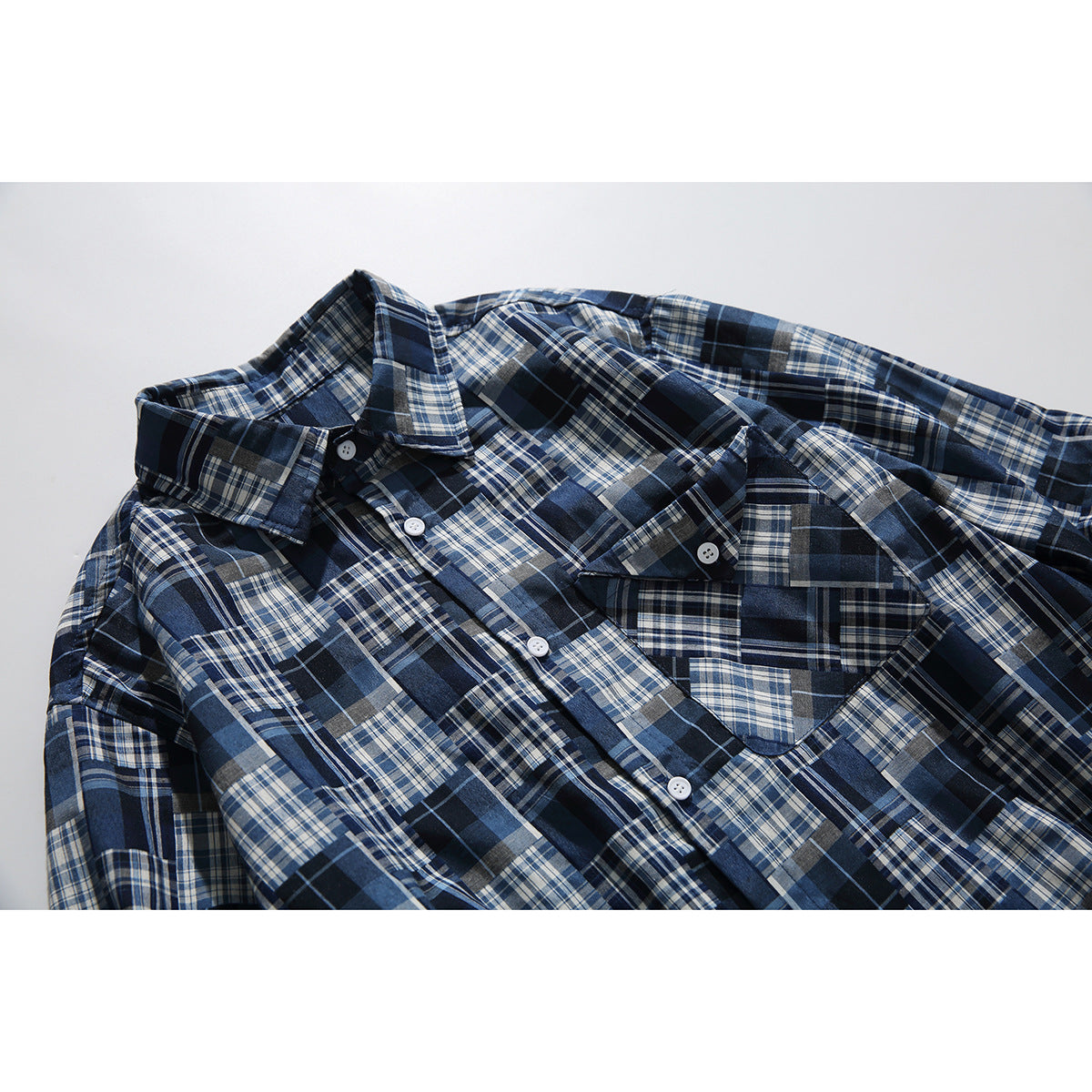 Angled flat lay of a navy, blue, gray, and white plaid button-up shirt with a pointed collar and chest pocket.