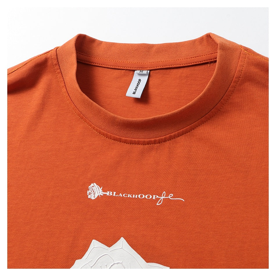 Close-up of an orange T-shirt neckline, collar label, and white chest lettering and graphic.
