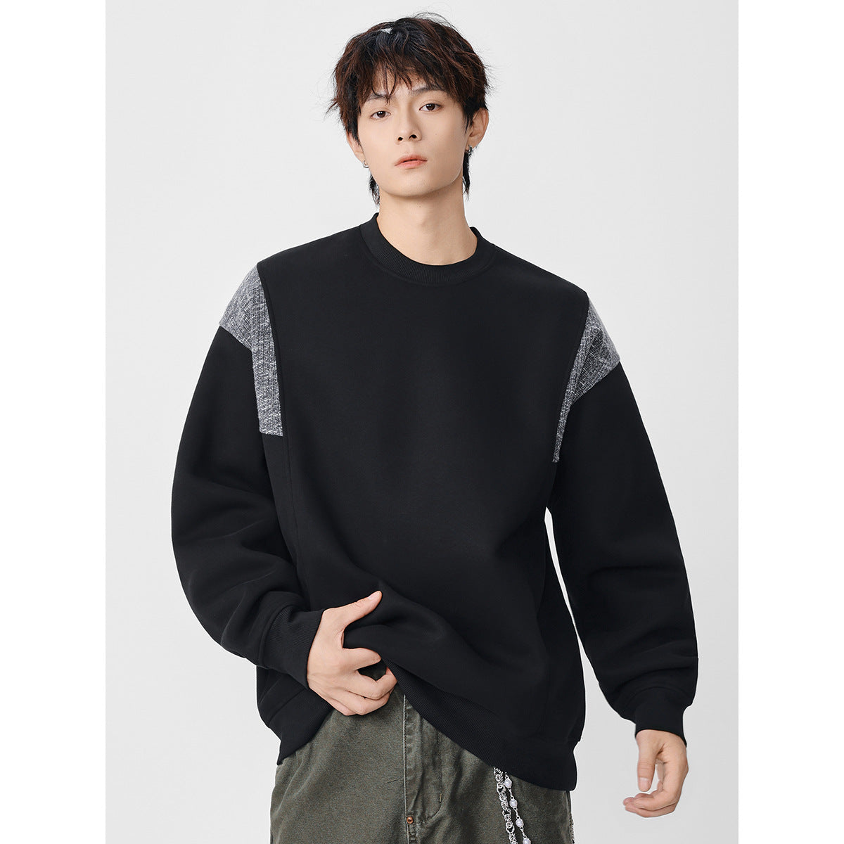 Front view of a model wearing an oversized black crewneck sweatshirt with textured gray shoulder panels.