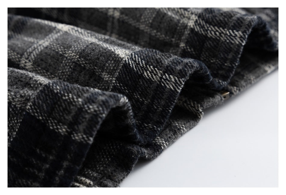 Close-up of folded edges and stitching on black and gray plaid fabric, with a small metal hardware piece visible.