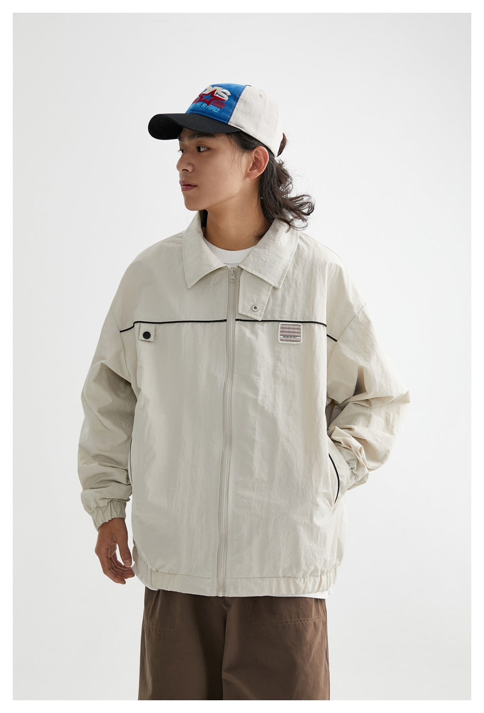Model wearing an ivory zip-front jacket with a pointed collar, black chest piping, snap tab, and elastic cuffs and hem.