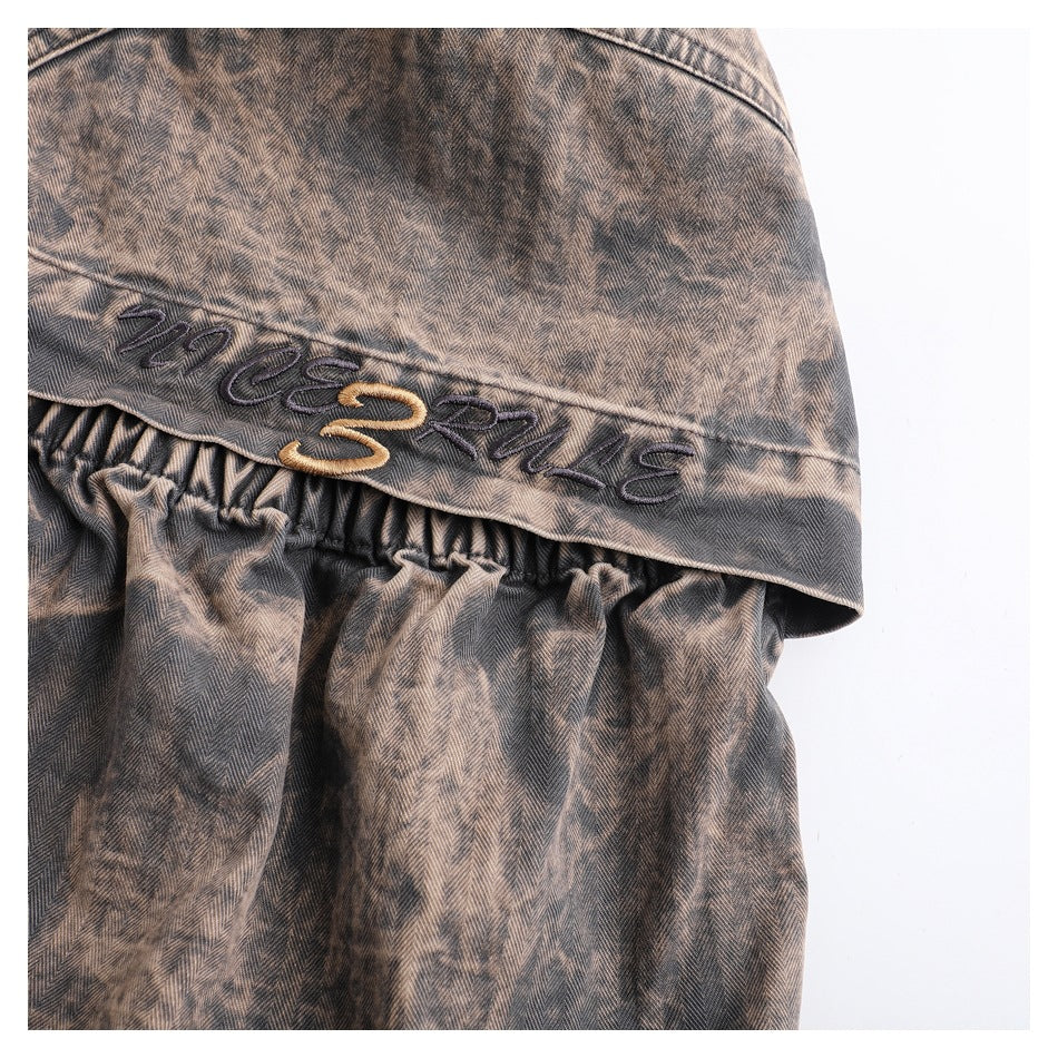 Close-up of brown herringbone fabric with embroidered lettering above a gathered section.
