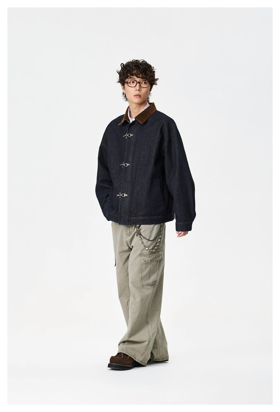 Full-length model wearing a dark indigo jacket with a brown collar and silver toggles, paired with loose khaki cargo pants.