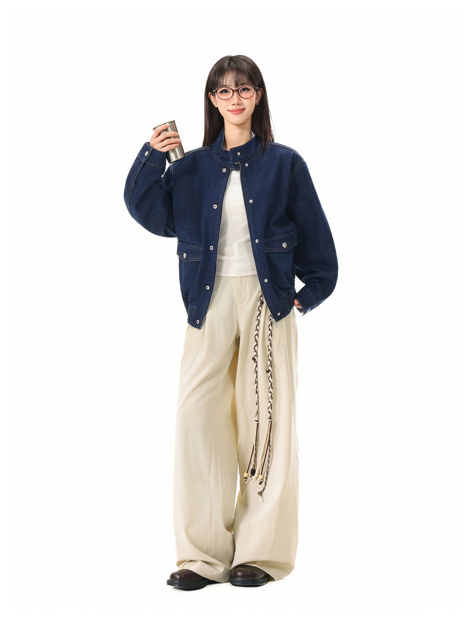 Model wearing the blue denim-look jacket open over a white top and wide-leg cream trousers, holding a metal cup