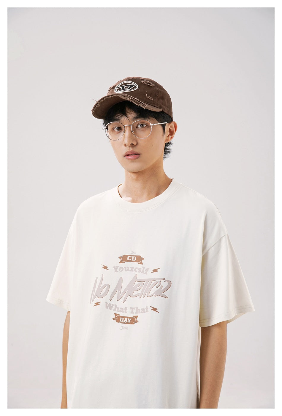Close view of a model wearing an oversized ivory T-shirt with a large brown and taupe English graphic on the chest.