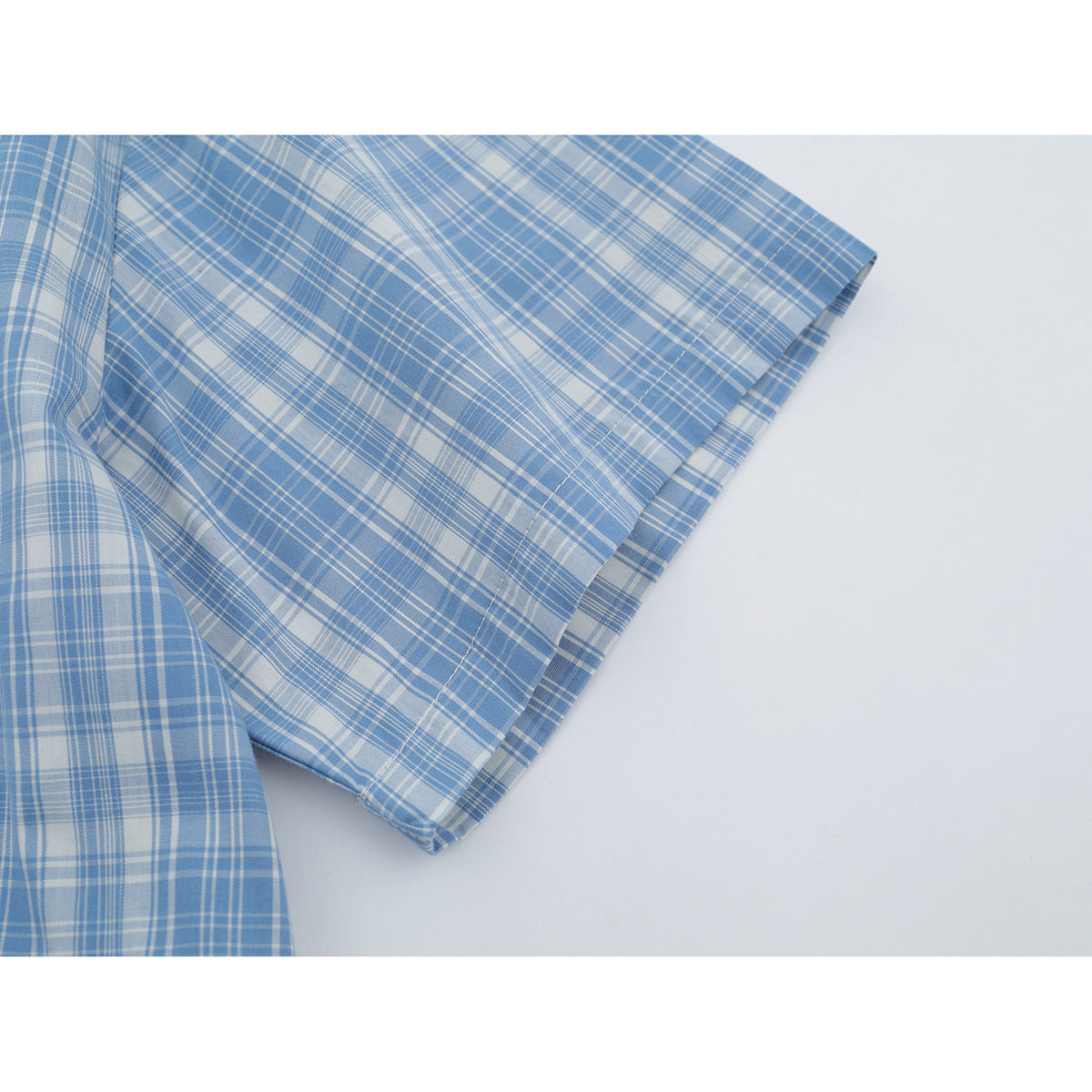 Close-up of the short sleeve and stitched hem of a light blue and white plaid shirt.