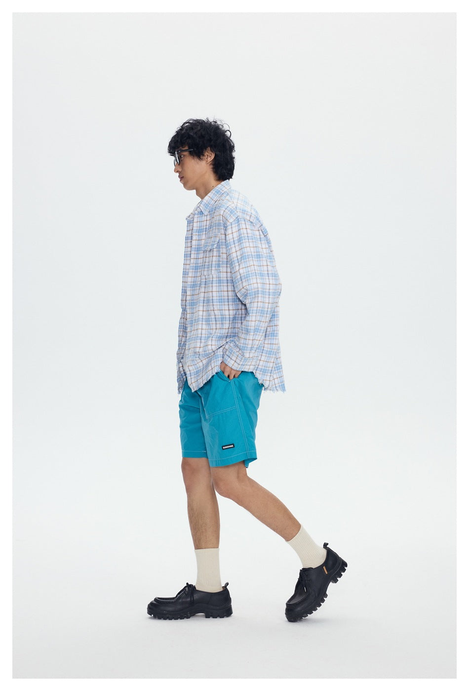 Side view of a model wearing a blue-and-tan plaid shirt and turquoise shorts.