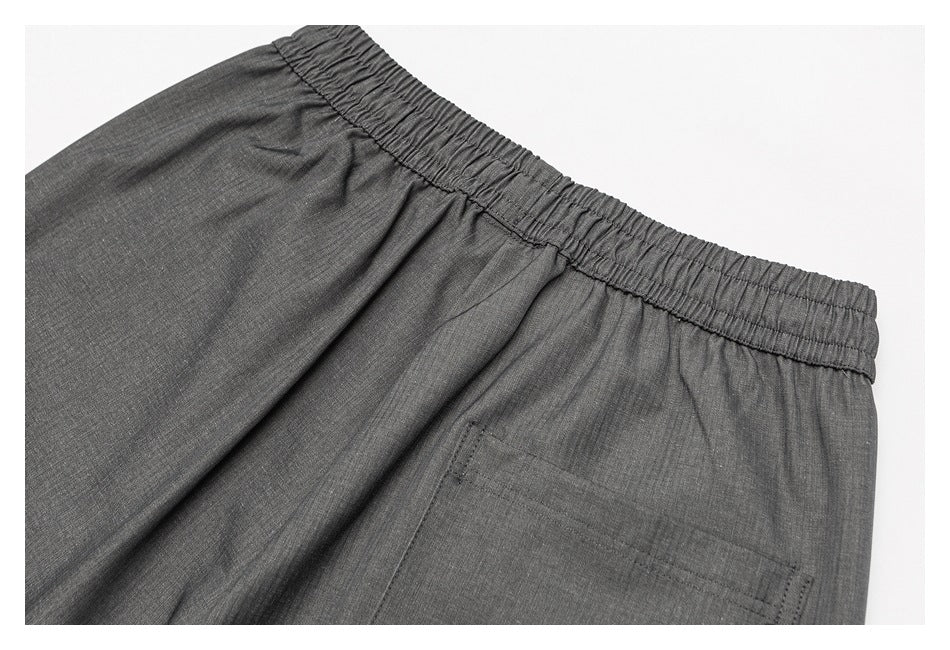 Close-up of dark gray trousers showing the gathered elastic back waistband and a patch pocket.