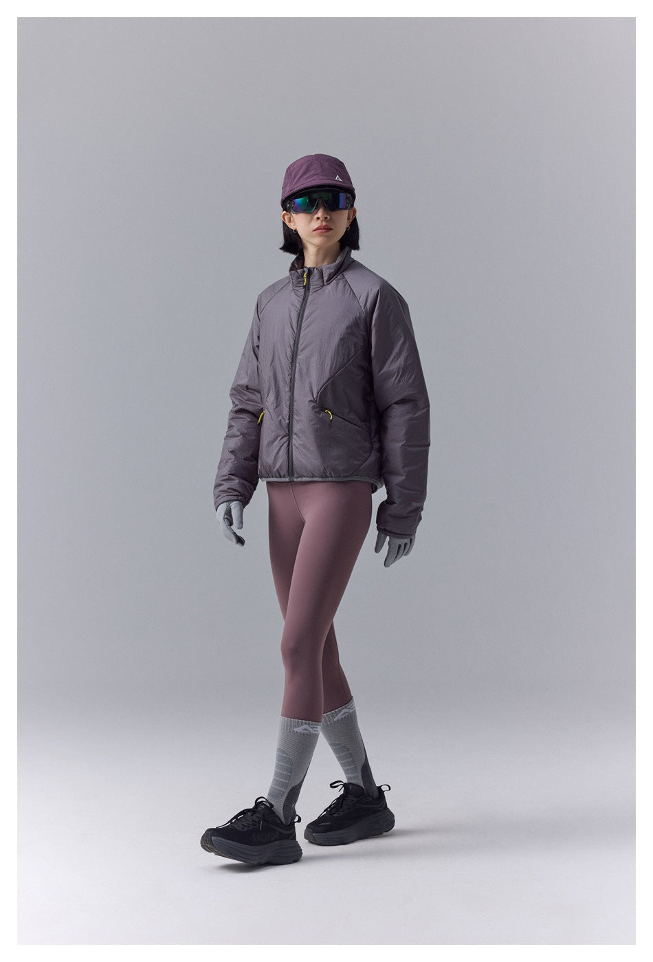 Full-length front view of a model in a gray-plum zip jacket, mauve leggings, gray gloves and socks, and black sneakers.
