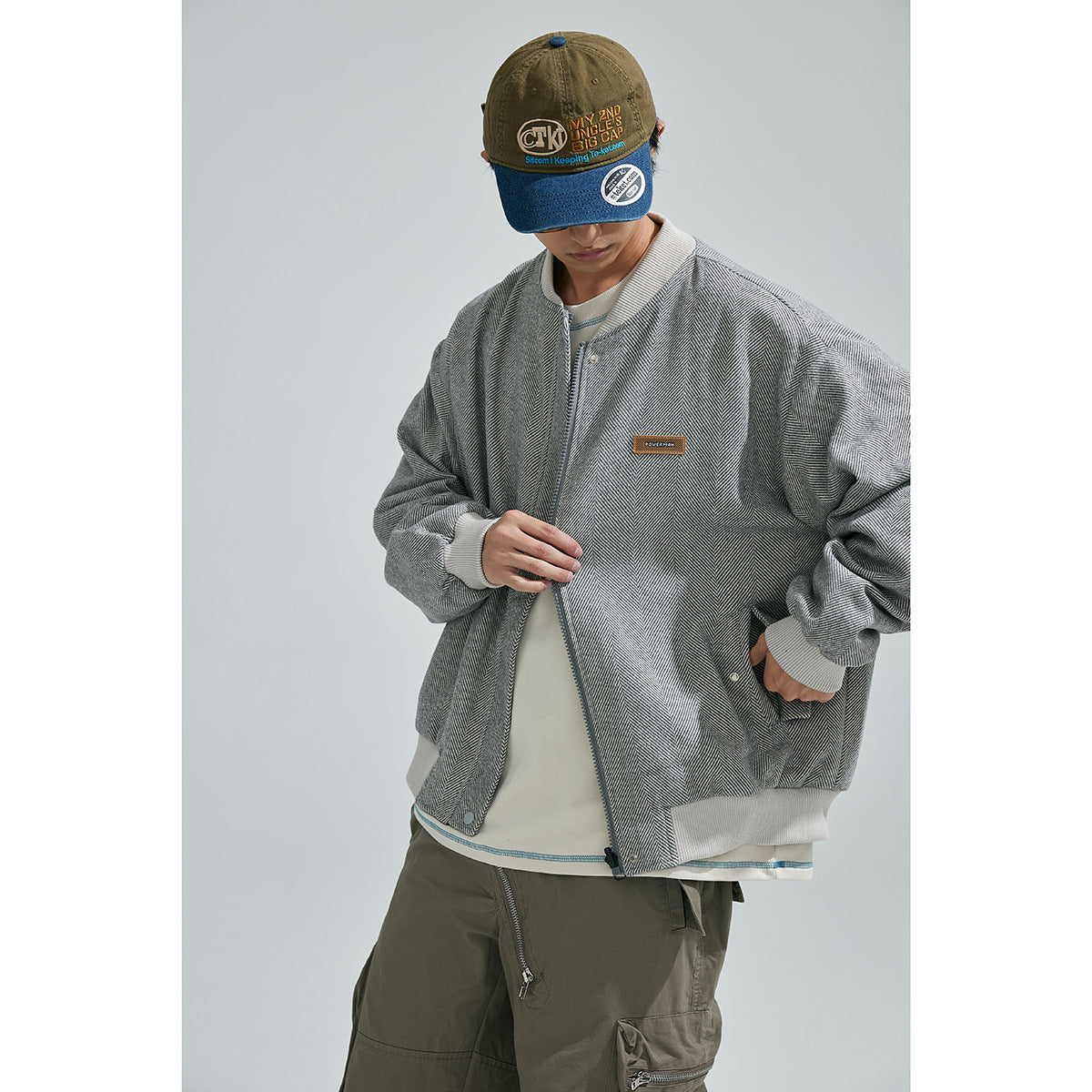Model wearing a gray herringbone bomber jacket with ribbed trim and a white shirt; close view of the front.