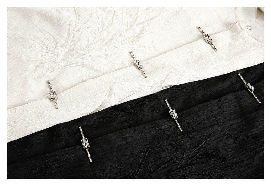 Close-up of ivory and black shirt fabric with embroidered motifs and silver-tone decorative fasteners.
