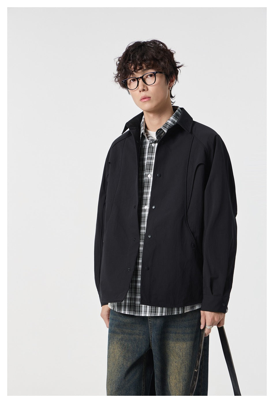 Model wearing black snap-front shirt jacket open over a plaid shirt, three-quarter view