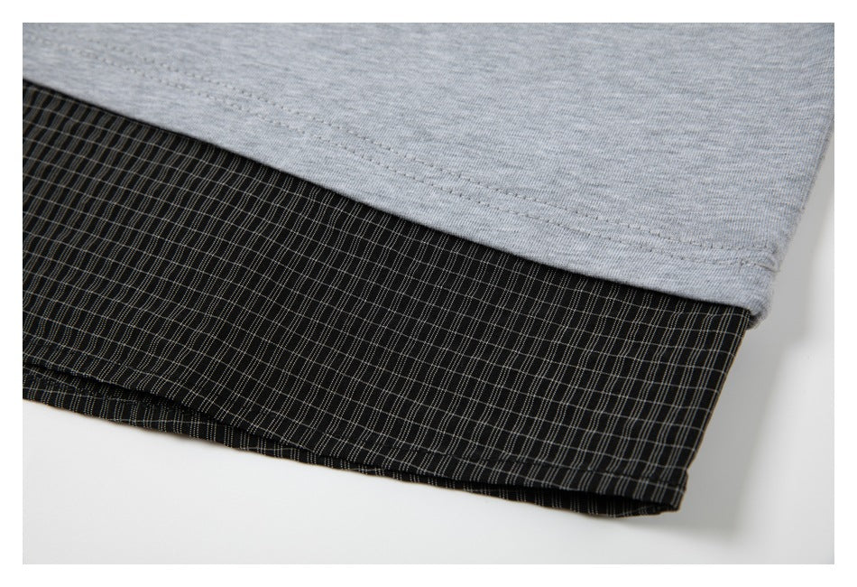 Close-up of a gray garment hem layered over black fabric with a fine plaid pattern.