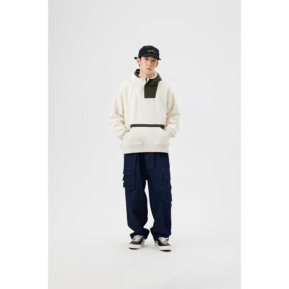 Front view of a model in an ivory pullover hoodie with an olive hood panel and front pocket.