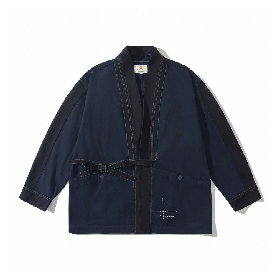 Navy blue kimono-style jacket with dark contrast trim, side tie belt, button-flap pockets and white stitched cross detail