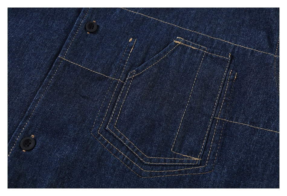 Close-up of a dark indigo denim shirt’s chest pocket, tan stitching, and two black buttons.