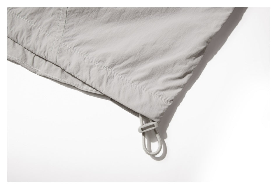Close-up of a pale gray garment hem with a looped drawcord and plastic toggle.