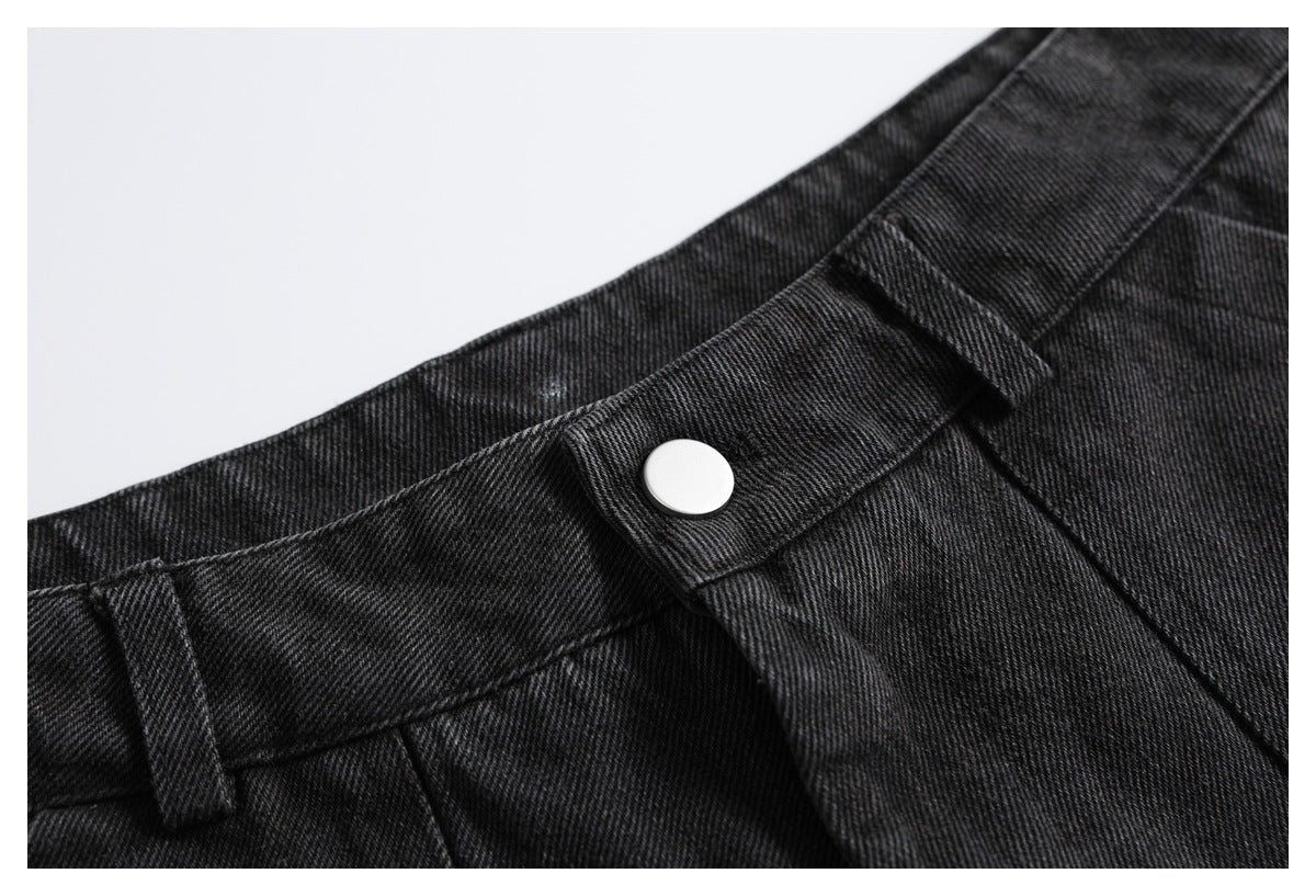 Close-up of charcoal-black denim trousers focused on the waistband, belt loop and silver button.