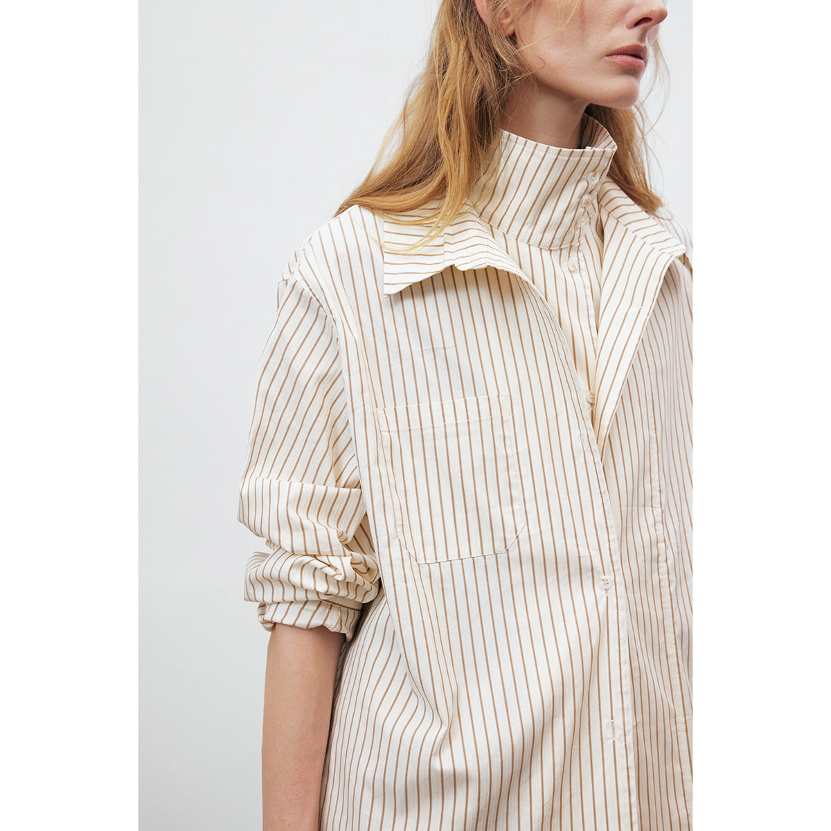 Close-up of an ivory and tan pinstriped shirt with a high buttoned collar, oversized lapels and chest pocket.
