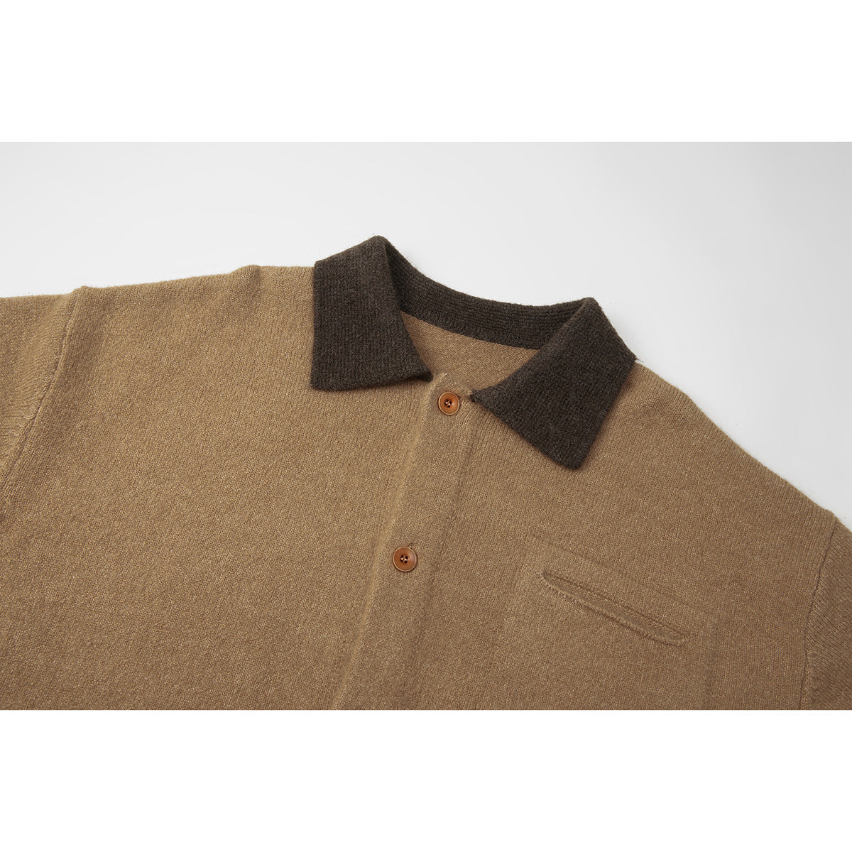 Close-up of a tan knit cardigan with a dark brown collar, brown buttons, and a chest pocket.