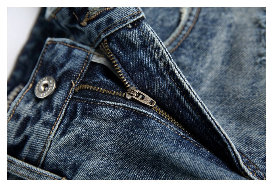 Close-up of a brass-tone zipper and button on blue denim jeans.