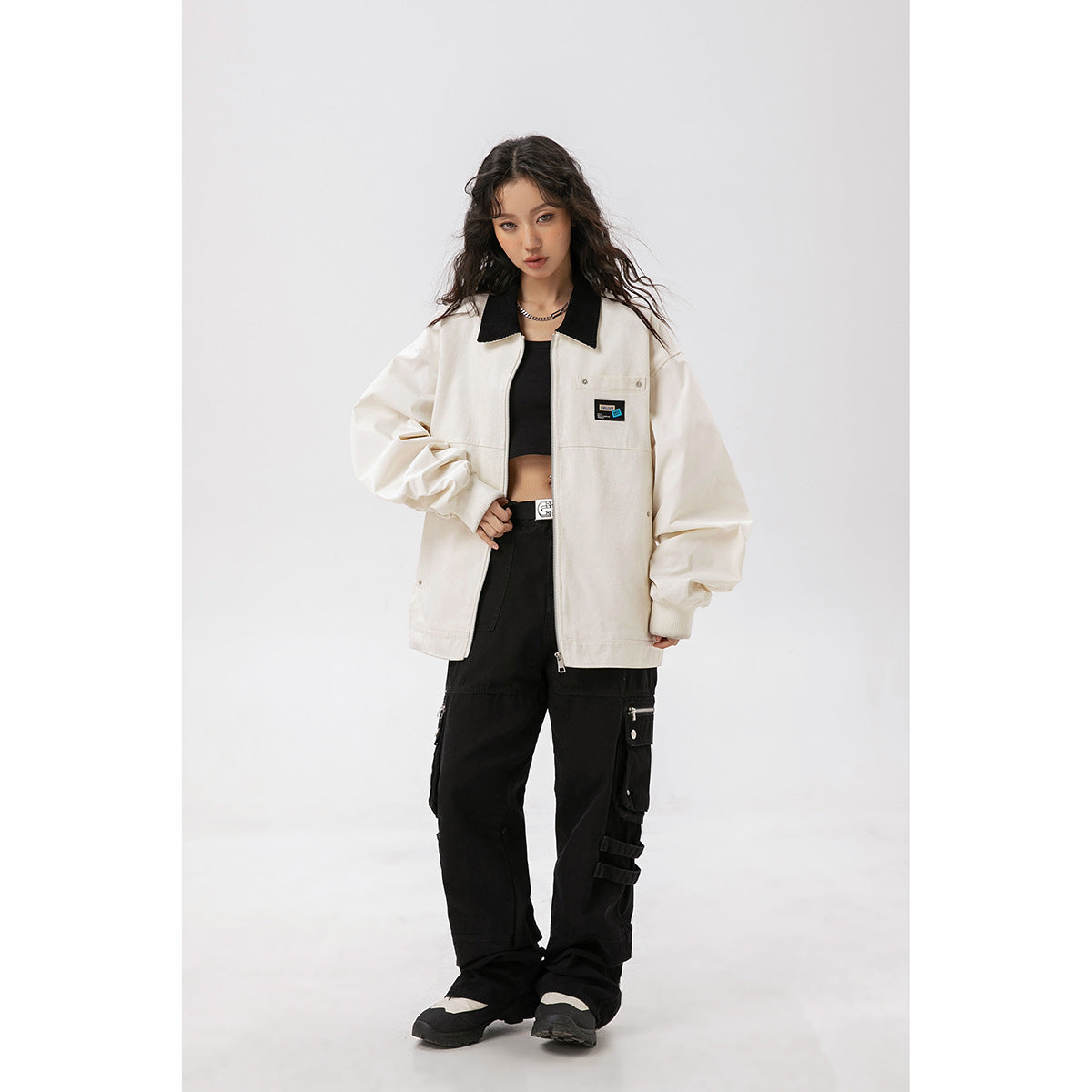 Model wearing an ivory zip-front jacket with a black collar and chest patch, paired with black cargo pants.