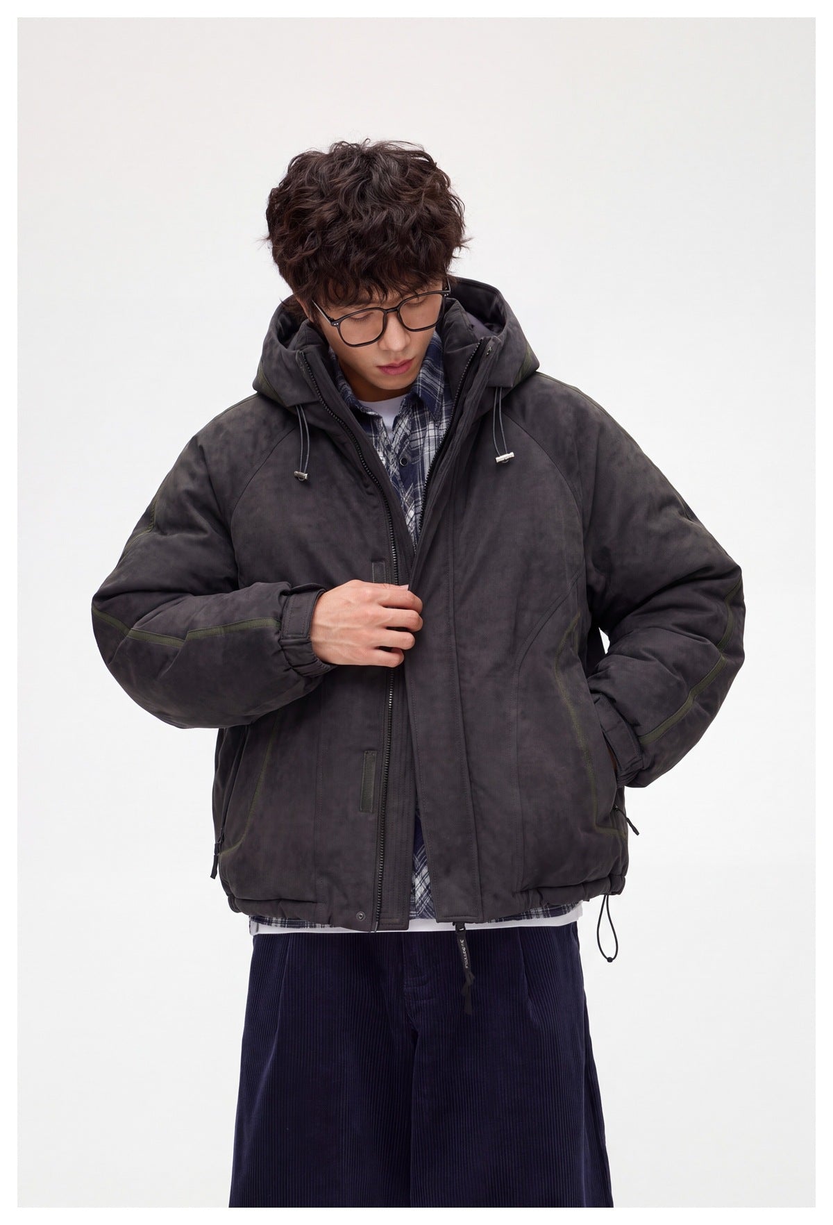 Model adjusting the front of a charcoal hooded jacket, showing its zipper, sleeve details, and roomy fit.