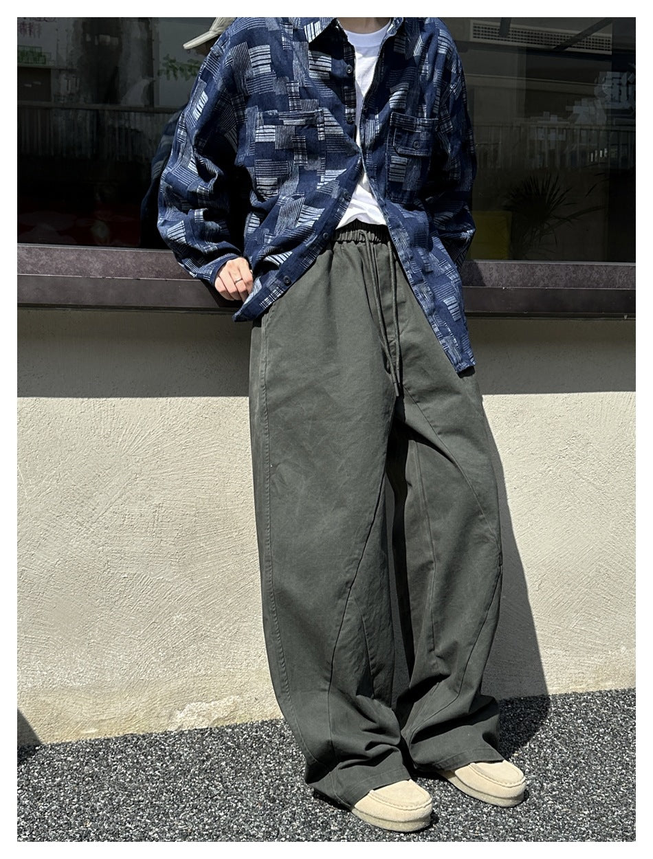 Model wearing dark olive wide-leg drawstring pants, shown with a blue patterned button-up shirt.