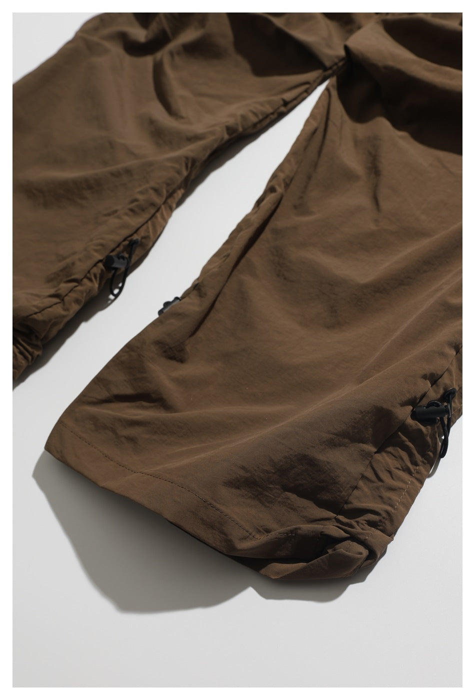 Close-up of brown shorts leg hems with black adjustable drawcord toggles.