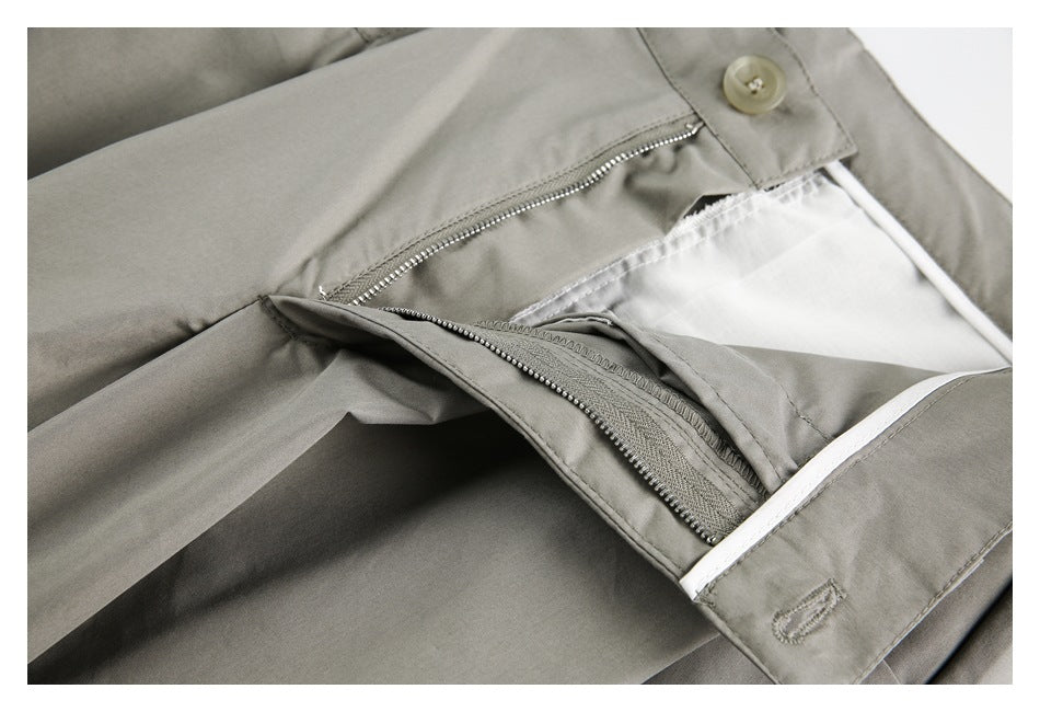 Close-up of taupe-gray trousers with the front fly unzipped, revealing the zipper and white inner lining.