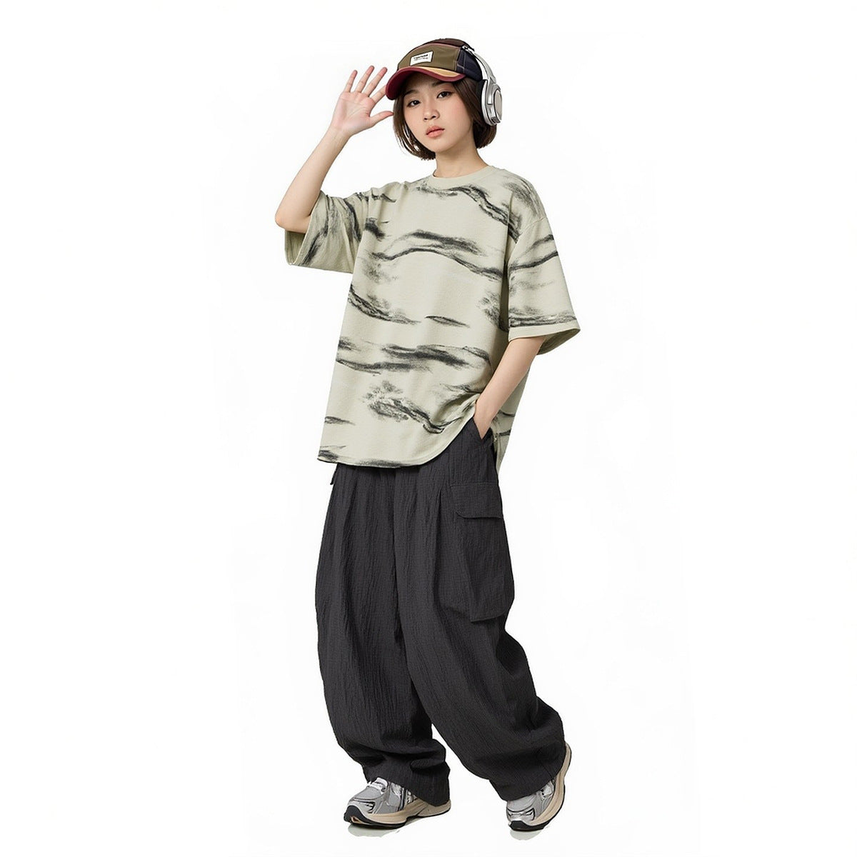 Model wearing an oversized cream T-shirt with dark brushstroke stripes and loose black cargo pants.