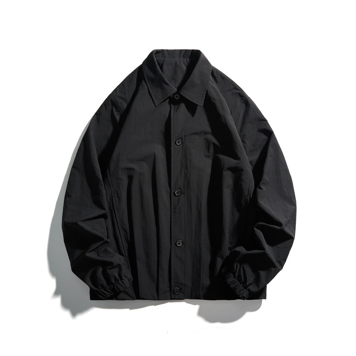 Black button-front jacket with pointed collar, elastic cuffs and black buttons, flat lay
