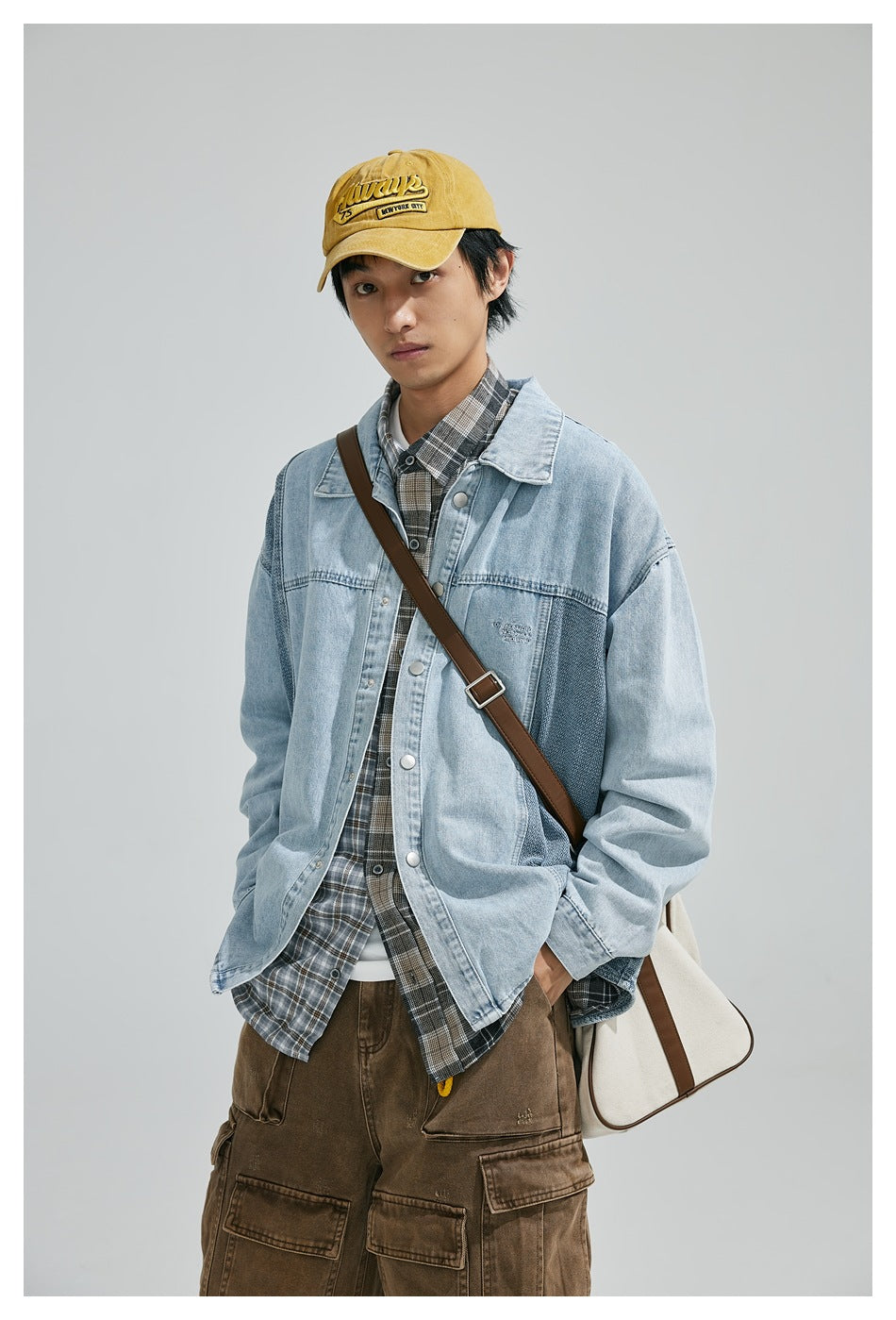 Front view of a model wearing a light-blue contrast-panel denim jacket over a plaid shirt, with brown cargo pants and a