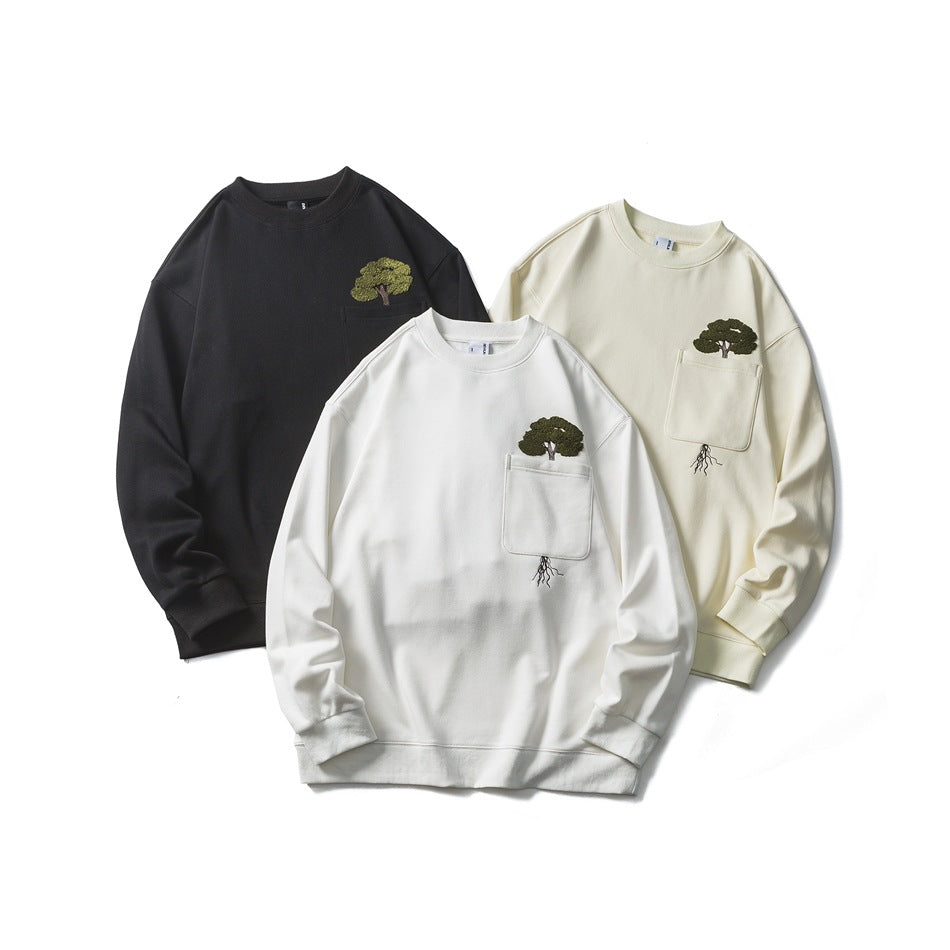 Three crewneck sweatshirts in black, white, and ivory, each with a chest pocket and tree embroidery.