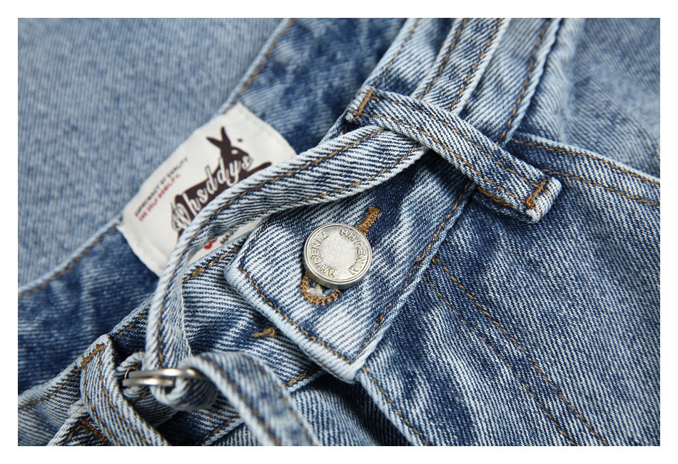 Close-up of light blue washed denim jeans showing the waistband, belt loops, button, and sewn label.