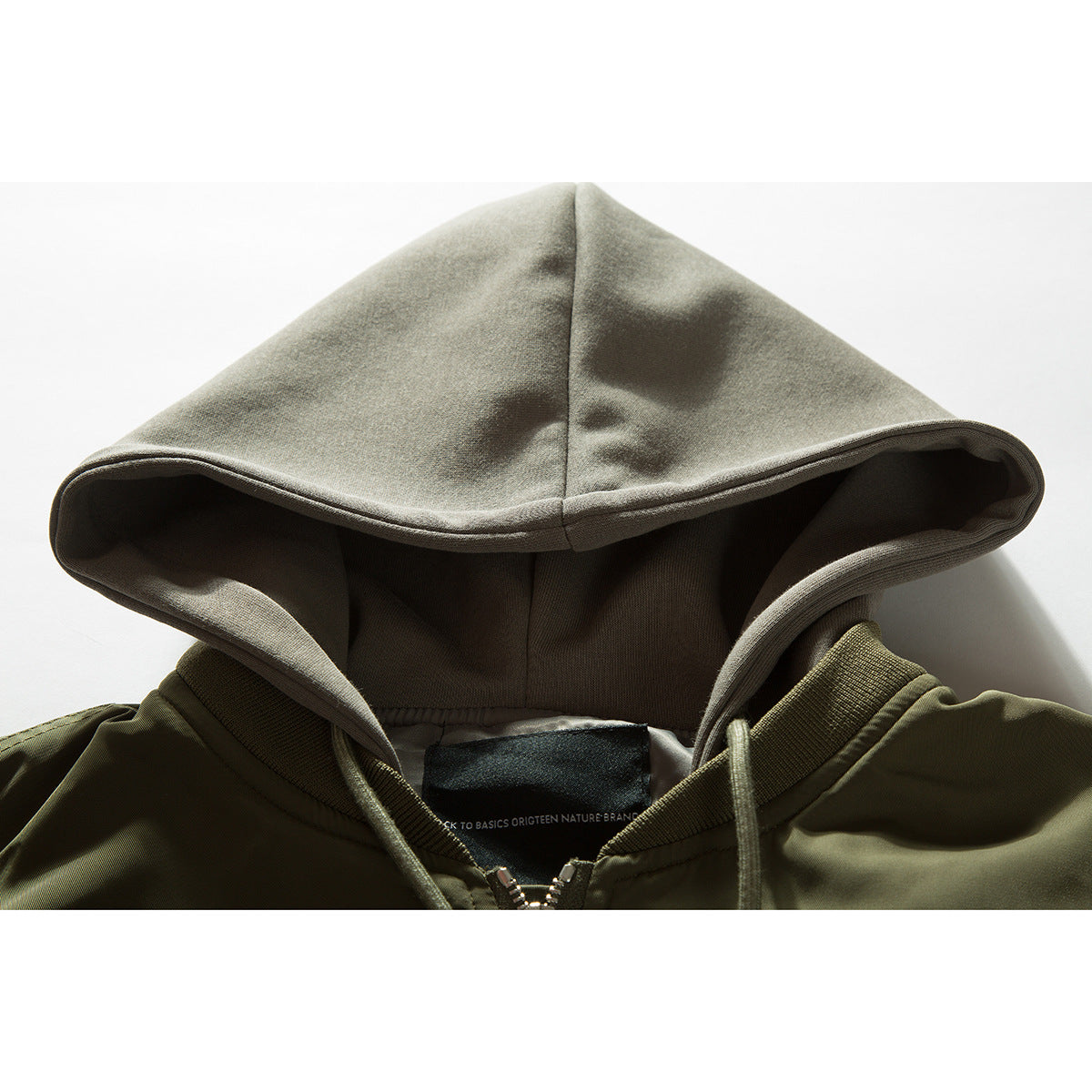 Close-up of an olive jacket collar and pale gray hood, showing the hood lining, drawstrings and neck label.