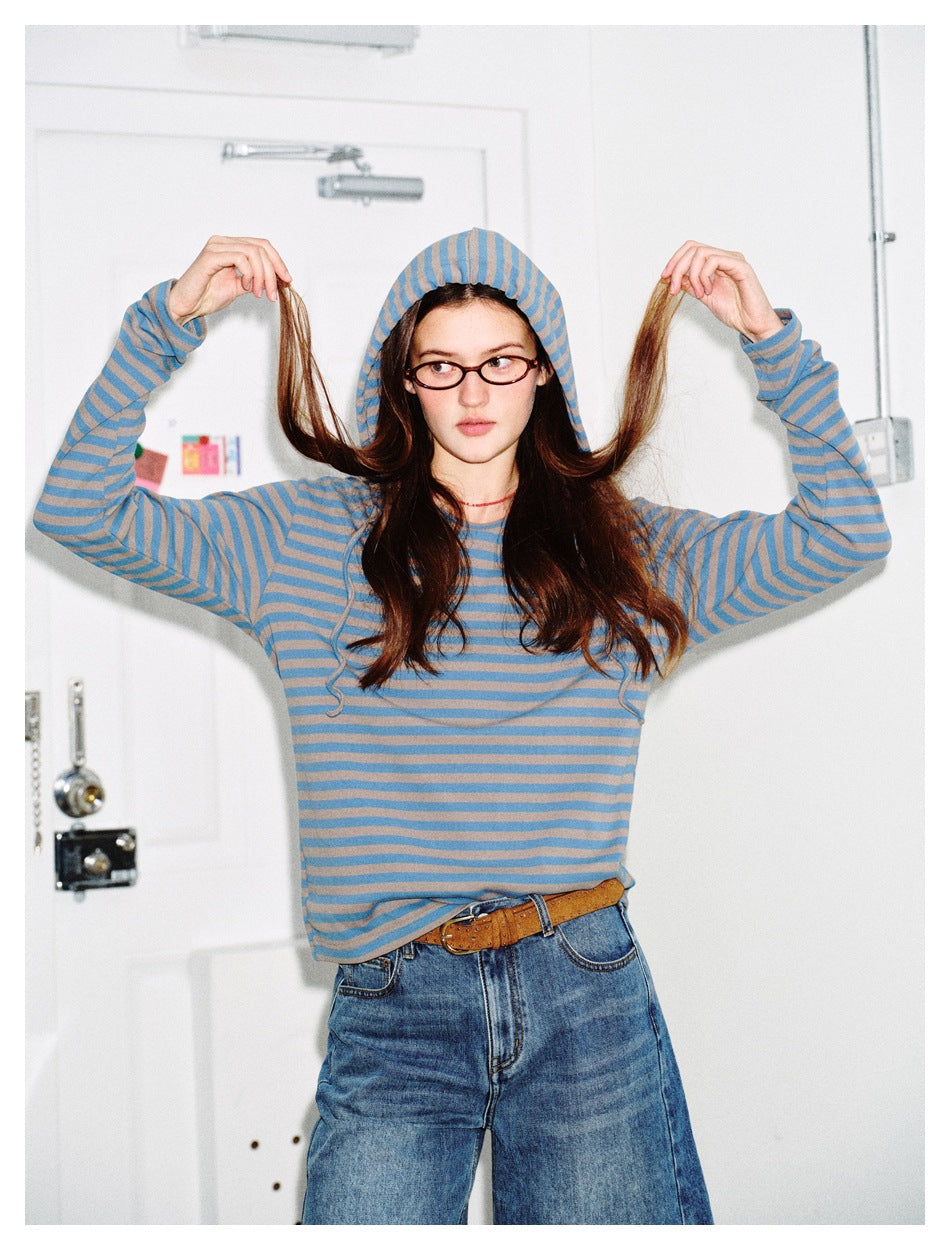 Model wearing a blue and taupe striped hooded long-sleeve top with jeans, lifting sections of her hair.