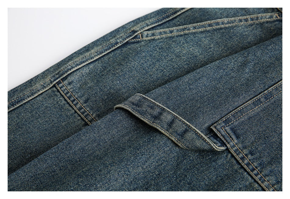 Close-up of the back pocket and yoke stitching on blue washed denim trousers.