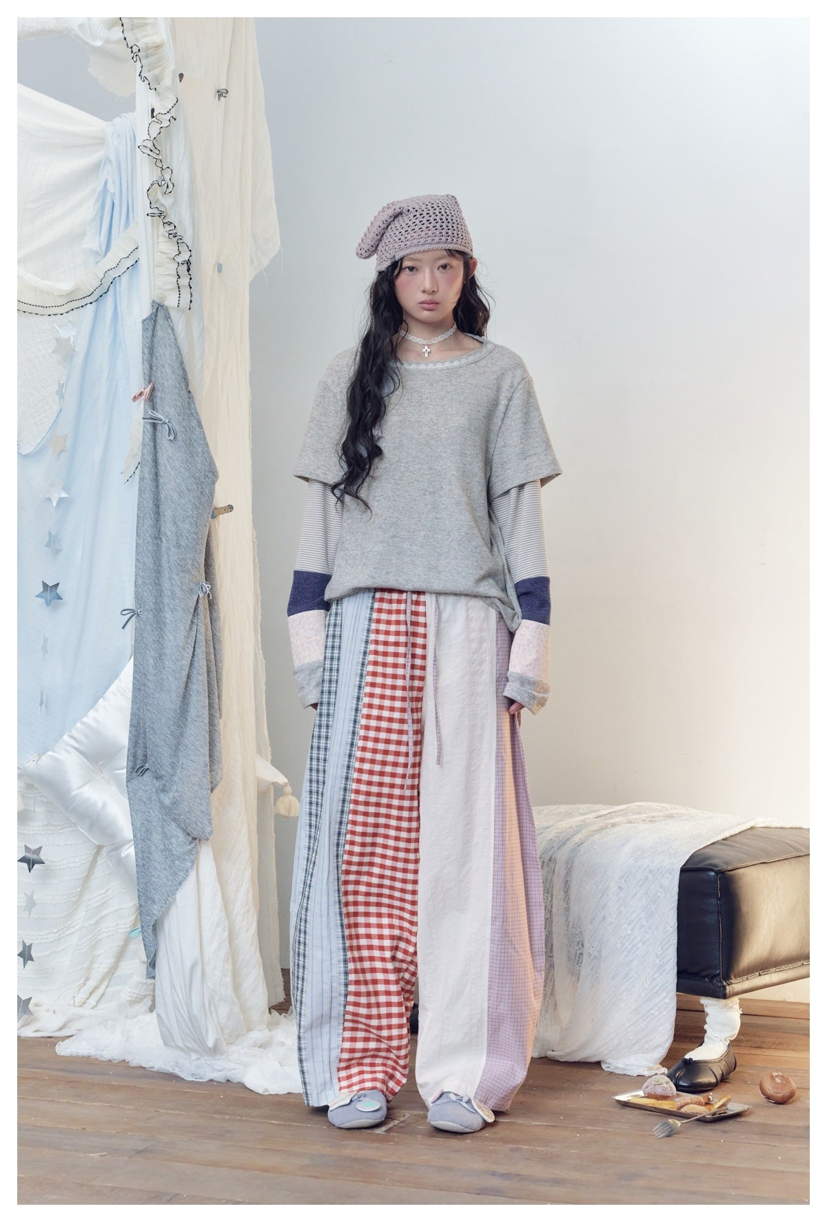 Model wearing patchwork plaid and gingham wide-leg pants with a gray layered top and crochet headscarf