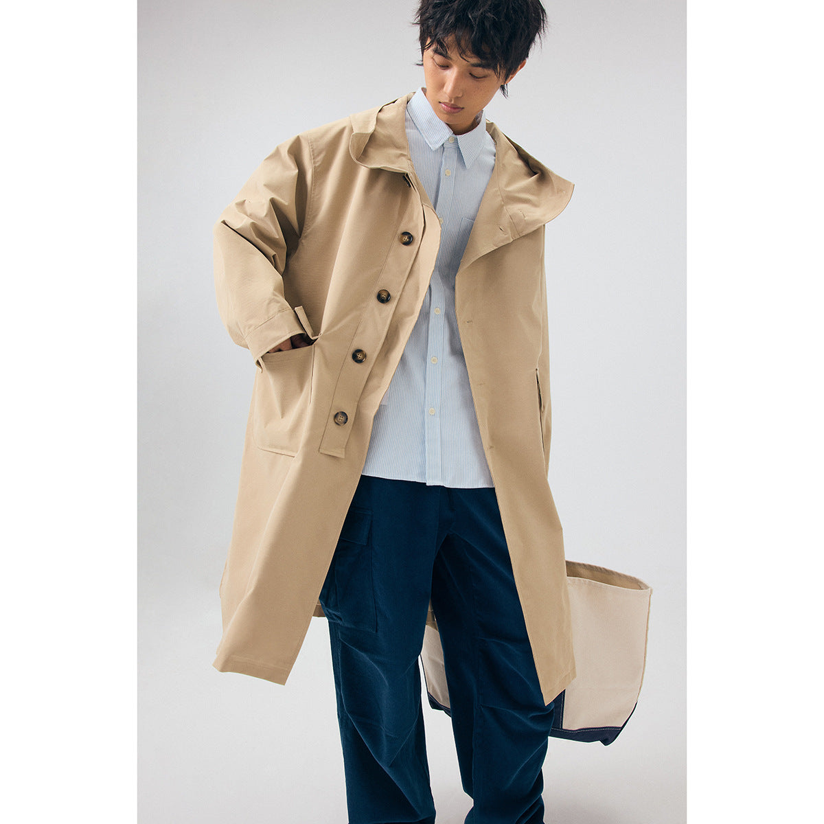 Model in an open beige hooded coat over a pale blue striped shirt and navy trousers.