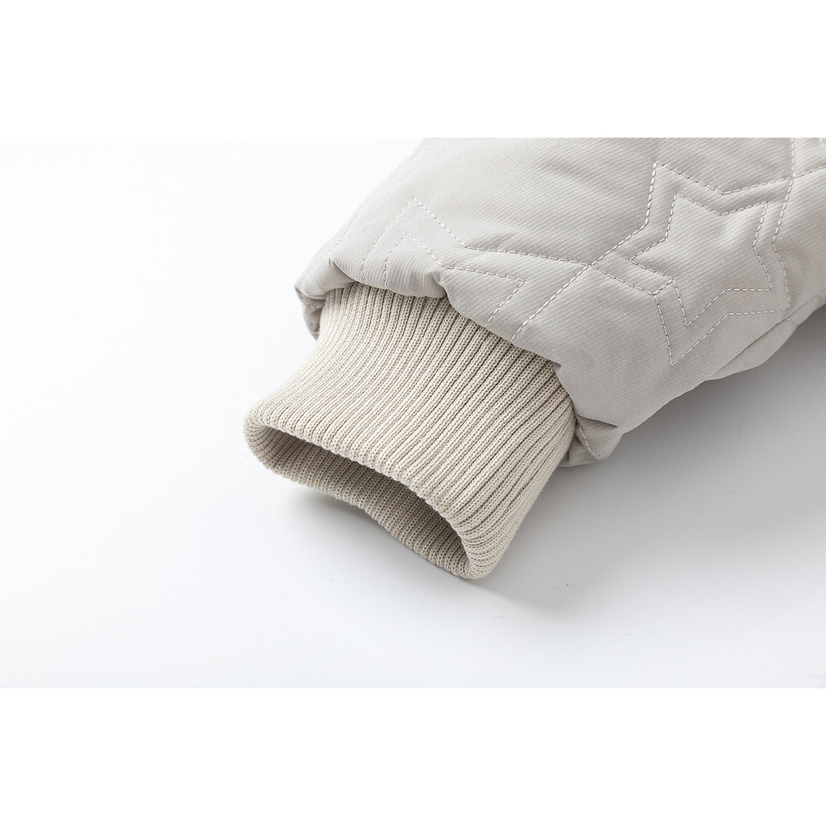 Close-up of a ribbed cream cuff beneath the star-quilted sleeve of a light gray jacket.