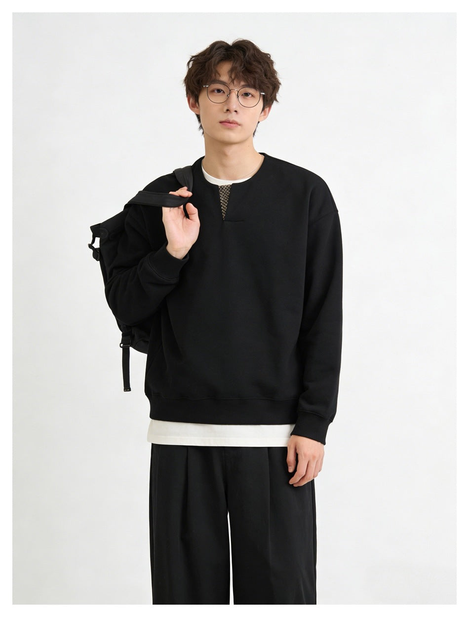 Person in black sweatshirt with checked neckline insert, holding a black backpack, with black pleated pants