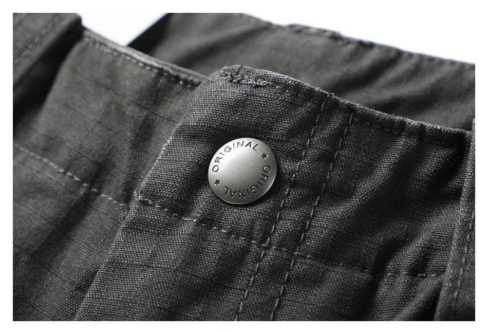 Close-up of a silver button engraved with “ORIGINAL” on charcoal trouser fabric.