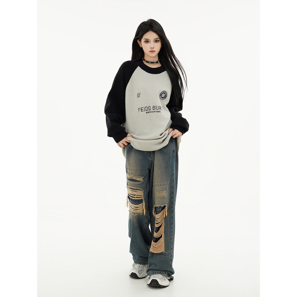 Model wearing an oversized light gray raglan sweater with black sleeves and chest graphics, paired with distressed wide-leg