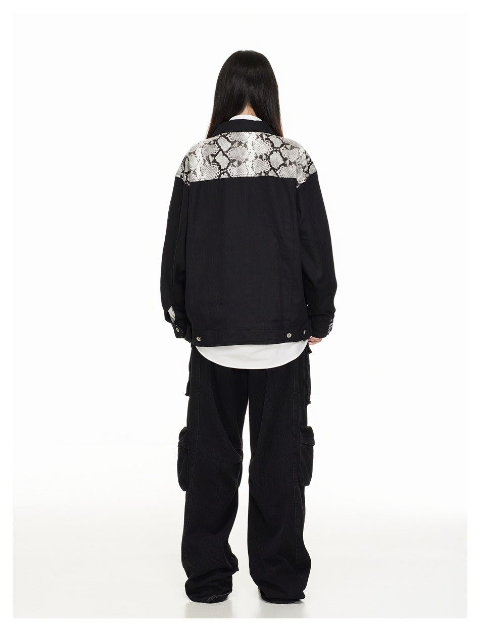 Rear view of a model wearing a black jacket with a snakeskin-patterned shoulder yoke and adjustable hem tabs.