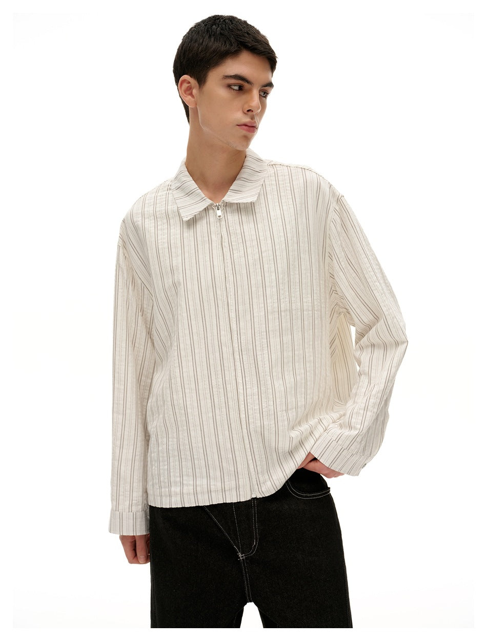 Model wearing an off-white thin-striped, long-sleeve shirt with a wide collar and front zipper, paired with black pants.