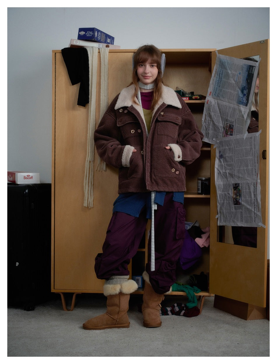 Model wearing a brown corduroy-textured jacket with fleece-like collar over layered clothing, standing by a wooden cabinet