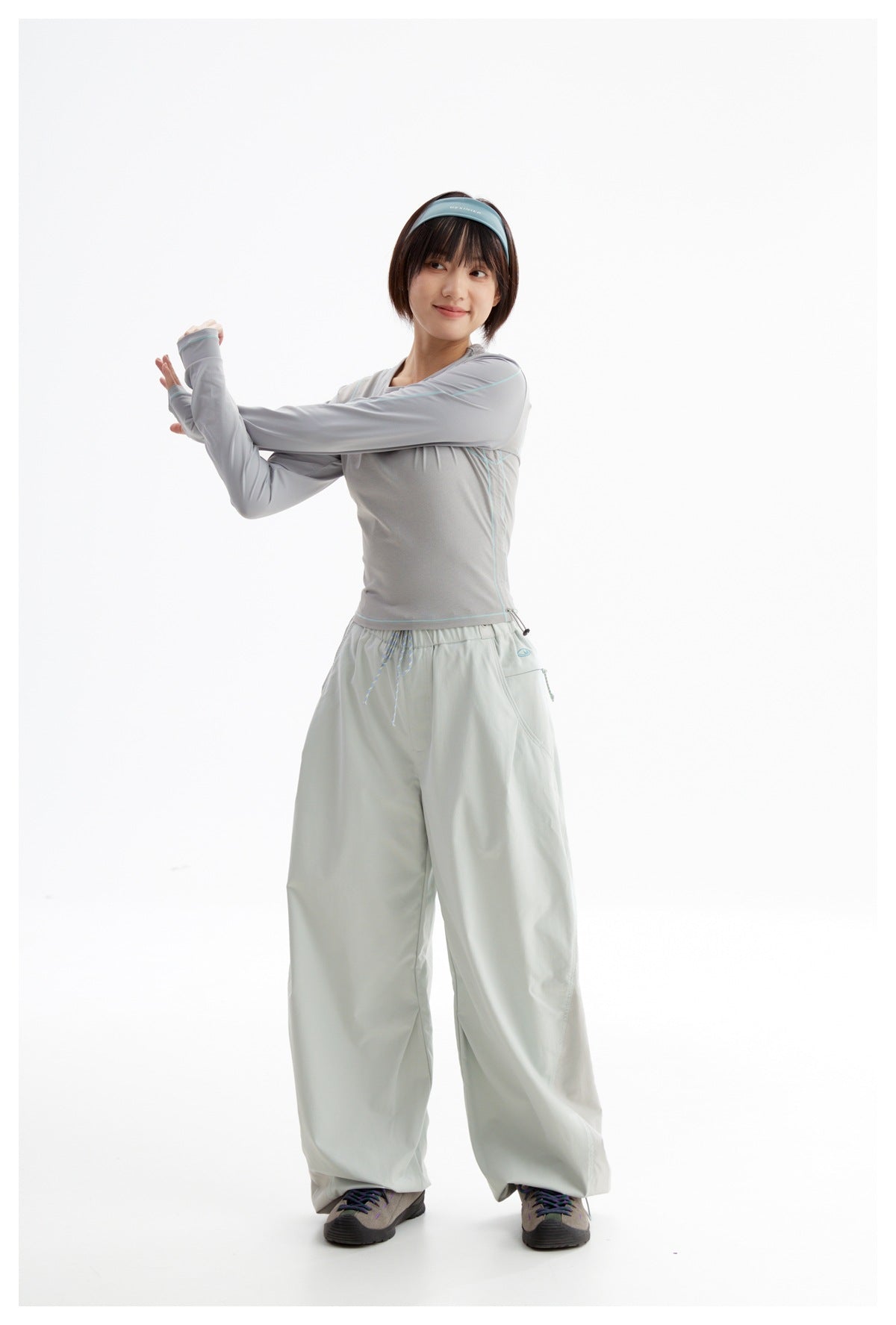 Model in a light gray top and pale mint wide-leg pants stretches one arm across her chest.
