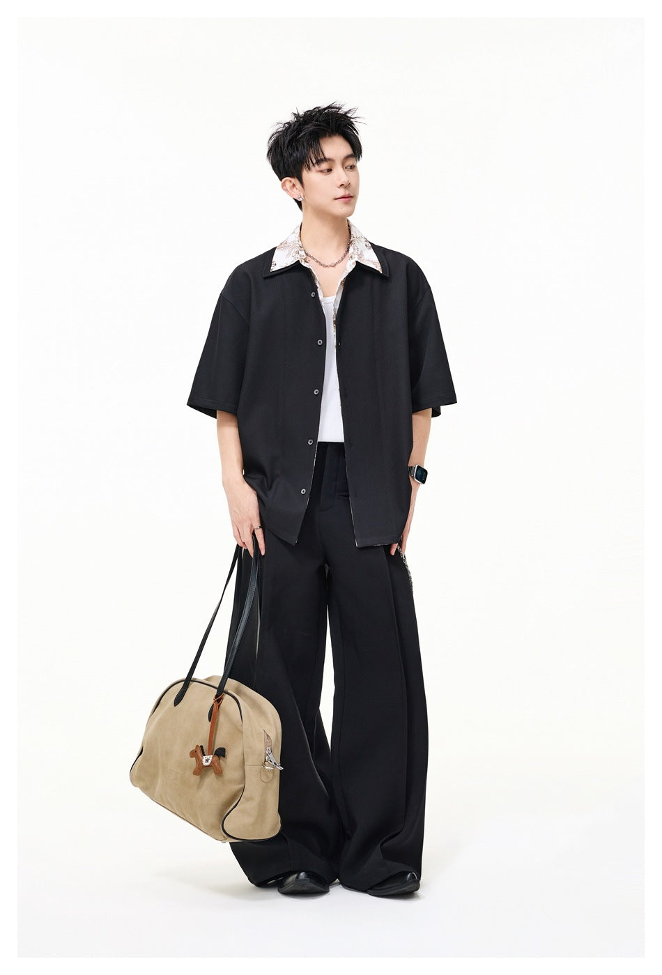 Full-length model wearing a loose black short-sleeve button-up with a light floral collar and wide-leg black trousers.
